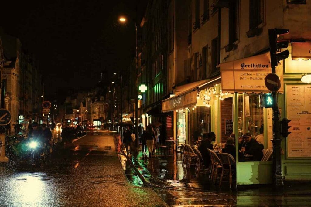 Foto de uma rua da cidade à noite com pessoas sentadas em mesas