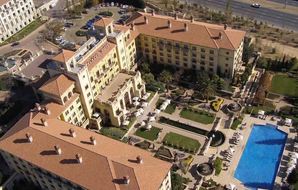 Foto da vista aérea de um edifício amarelo com uma piscina ao lado. 