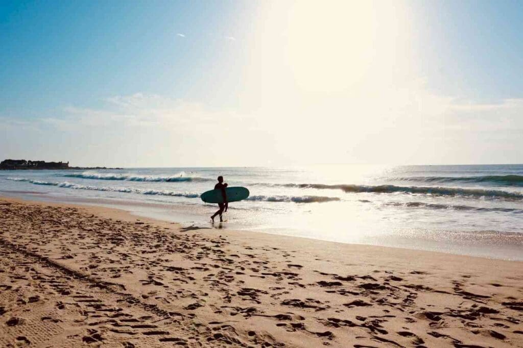 Foto de um surfista andando em uma praia com uma prancha de surf