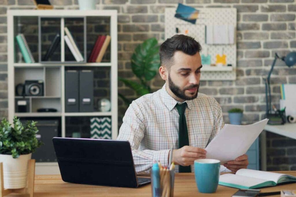 Foto de um homem sentado em frente a um computador enquanto lê