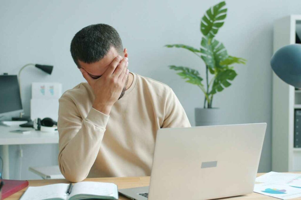 Foto de um homem esfregando o rosto na frente de um laptop